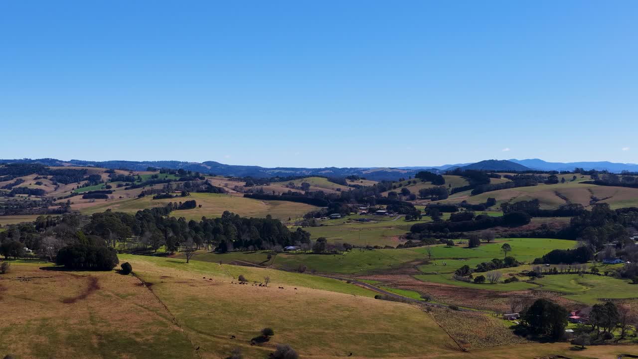 Drone ascends above rolling farmland under clear blue sky, revealing expansive rural landscape in daylight