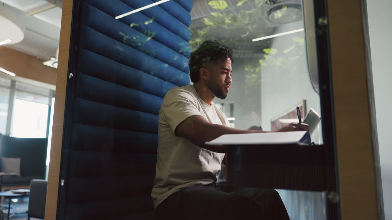 Young Man Concentrating While Writing in a Modern Office Booth