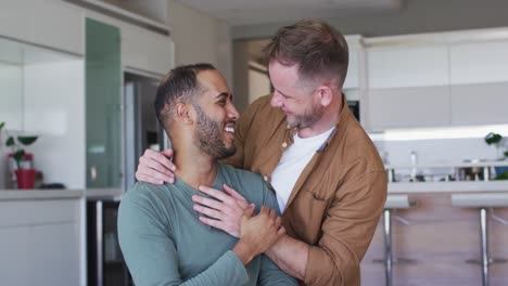 Multi-ethnic-gay-male-couple-talking-and-embacing-turning-to-camera-and-smiling