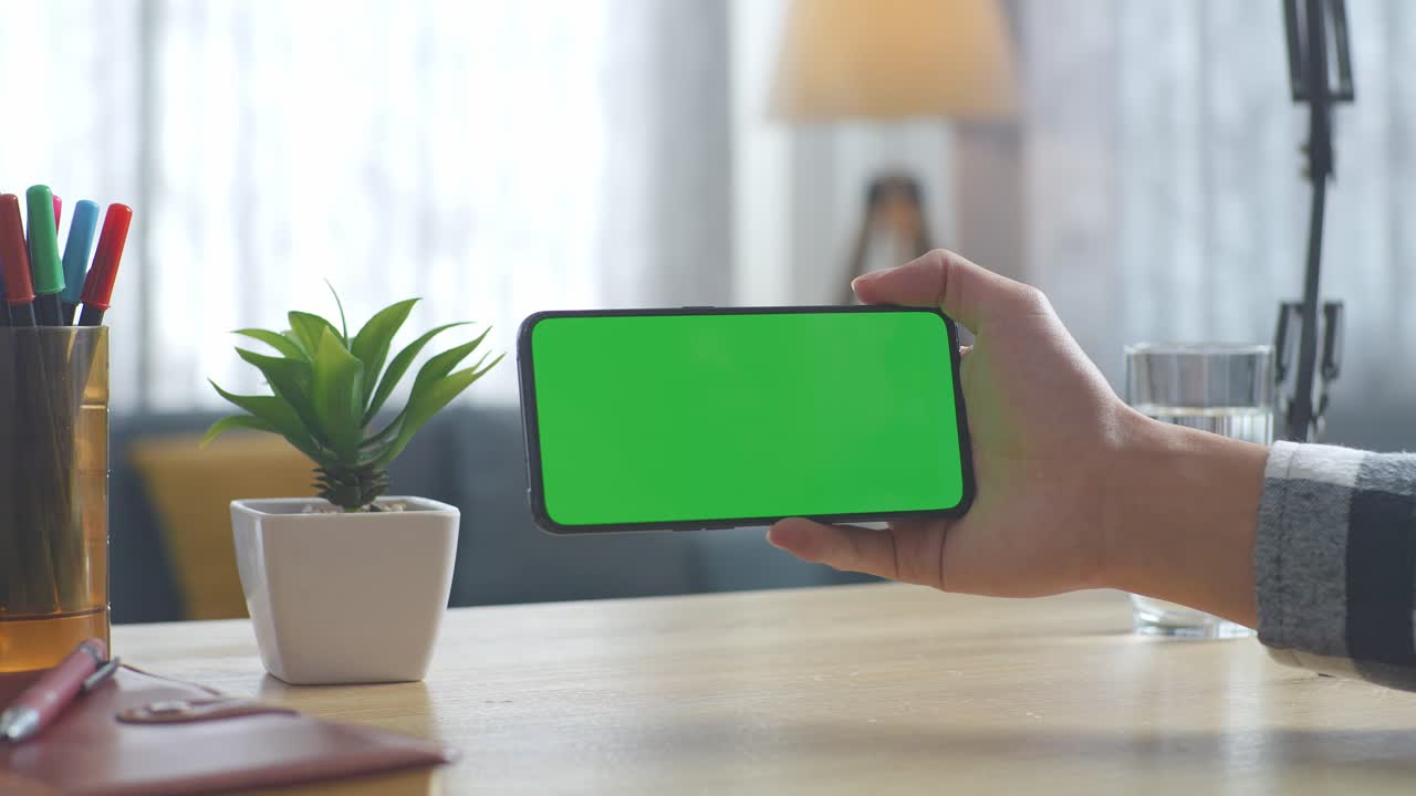 vista de arriba hacia abajo de una computadora portátil con pantalla verde simulada pantalla chromakey en un escritorio de oficina de madera al lado de la libreta con bolígrafos, gafas y un vaso de agua.
