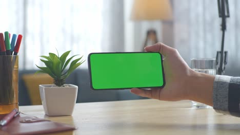 top down view of a laptop computer with mock up green screen chromakey display on a wooden office desk next to notebook with pens, glasses, and a glass of water. slow zoom out, close up