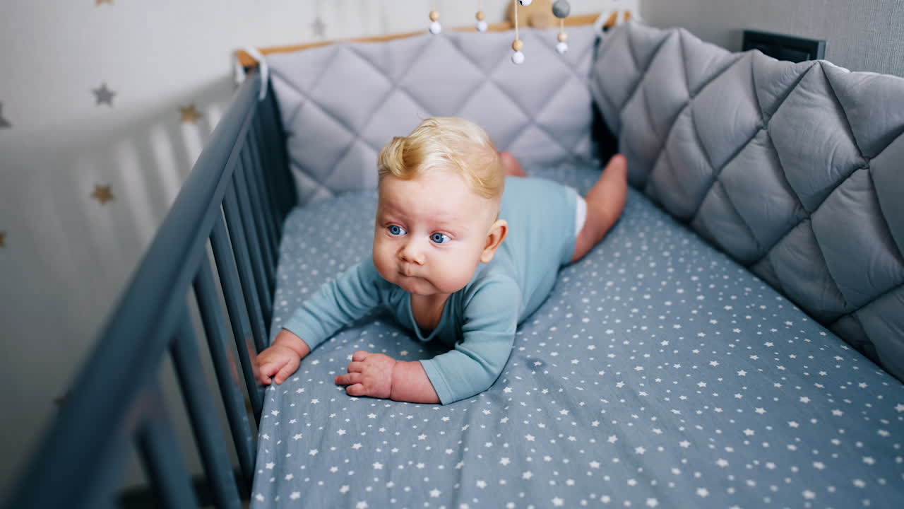 Adorable blue-eyed infant boy lying on his belly in the cot. Cute child with plump cheeks in the crib.