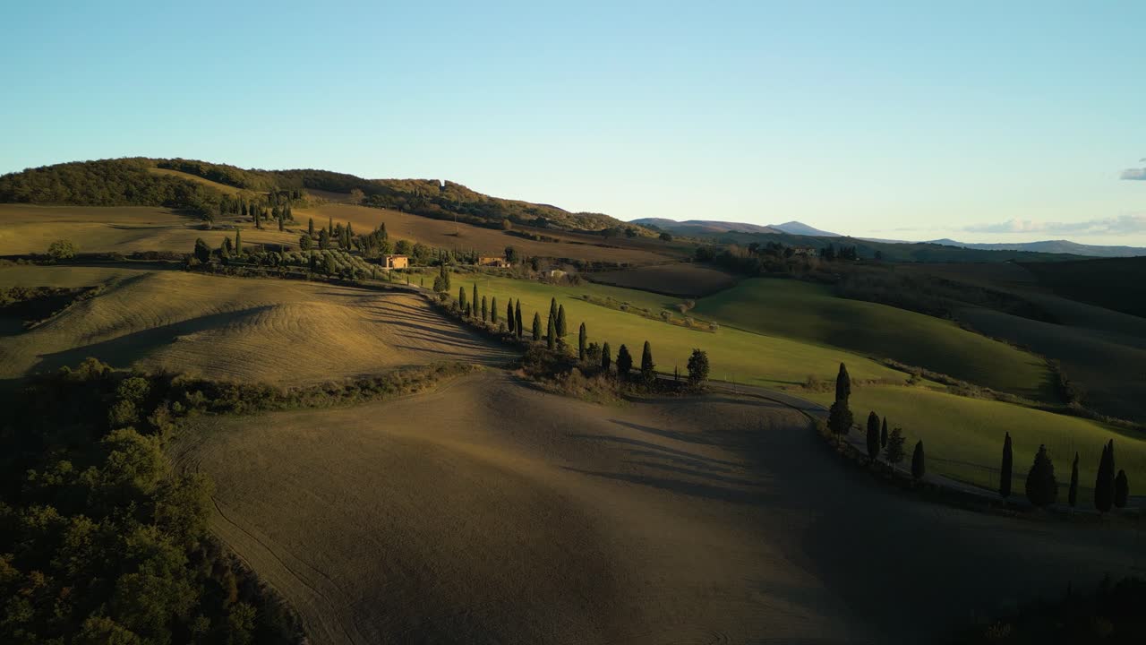 Sloping hills of Val d'Orcia Tuscany roll glowing green illuminated gold at sunset, aerial