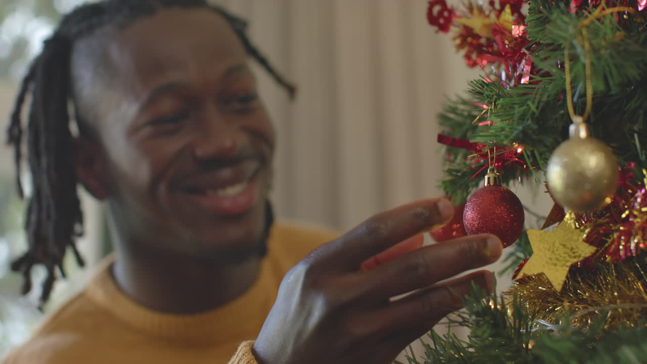 hombre afroamericano sonriente con dreadlocks decorando el árbol de navidad, en cámara lenta