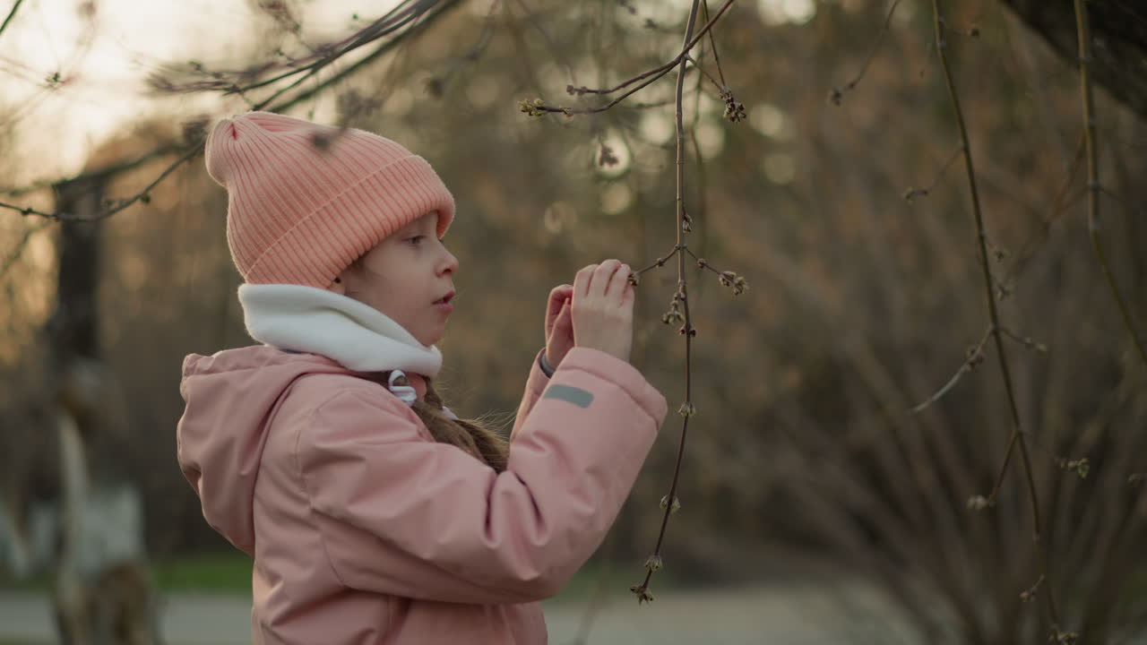 분홍색 재과 베니를 입은 어린 소녀가 건조한 나무 가지와 놀고, 호기심으로 자연 주변을 탐험하는 것을 볼 수 있습니다.