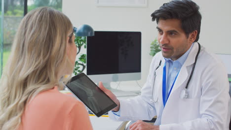 médico con bata blanca en la oficina mostrando una paciente femenina madura rayos x o escaneo en una tableta digital