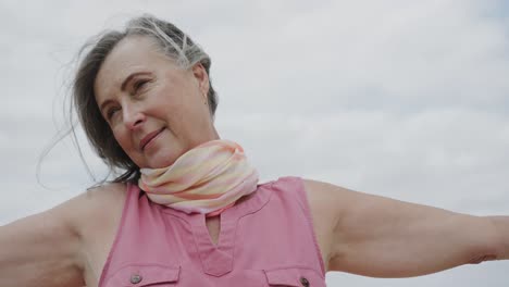 Happy-senior-caucasian-woman-with-arms-outstretched-smiling-against-cloudy-sky,-in-slow-motion