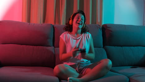 Young woman playing a video game sitting on the couch and winning the game