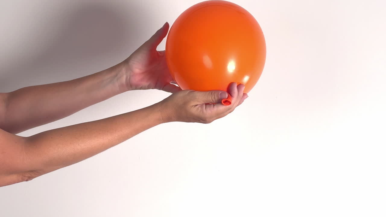 Hands Deflating an Orange Balloon Against a White Background