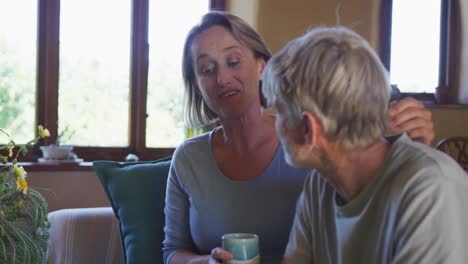 Lächelndes-älteres-Kaukasisches-Paar,-Das-Im-Wohnzimmer-Redet-Und-Kaffee-Trinkt