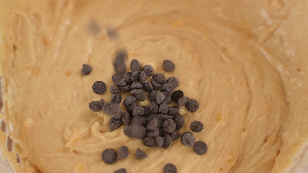las chispas de chocolate caen en masa de pan dulce, vista superior en cámara lenta