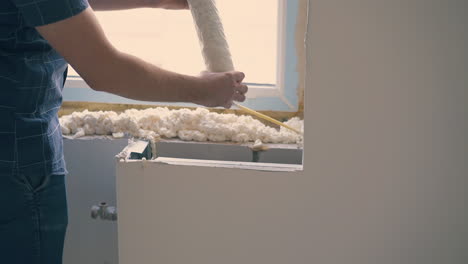 happy man applies spray foam insulation on sill in room