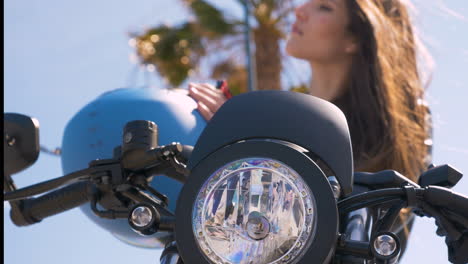 young woman sitting on motorcycle putting on helmet