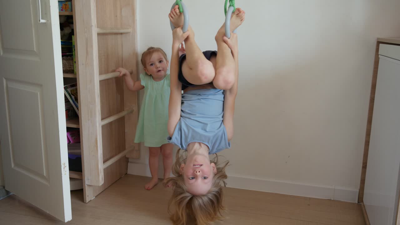 Bambina felice appesa a testa in giù agli anelli da ginnastica