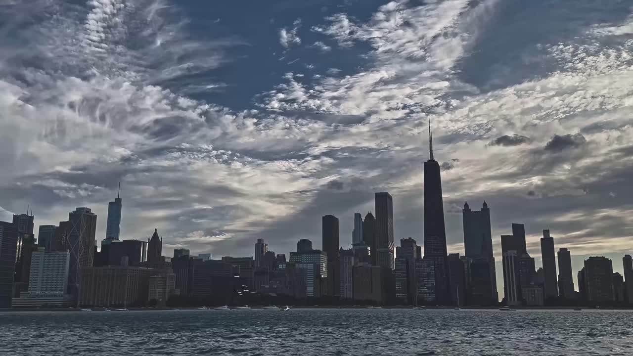A wide shot of the Chicago skyline with dramatic clouds rolling above the skyscrapers, viewed from Lake Michigan's edge.