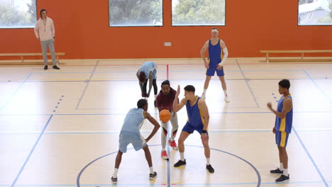 multiracial male basketball players in gym and throwing ball into basket with male coach