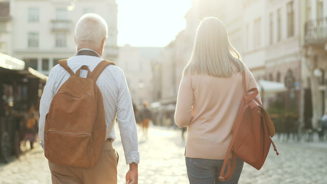 배낭을 메고 도시 거리를 걷고 화창한 날 이야기를 나누는 노인 부부의 뒷모습