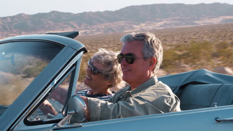 una pareja de ancianos conduciendo en un coche abierto en una carretera del desierto