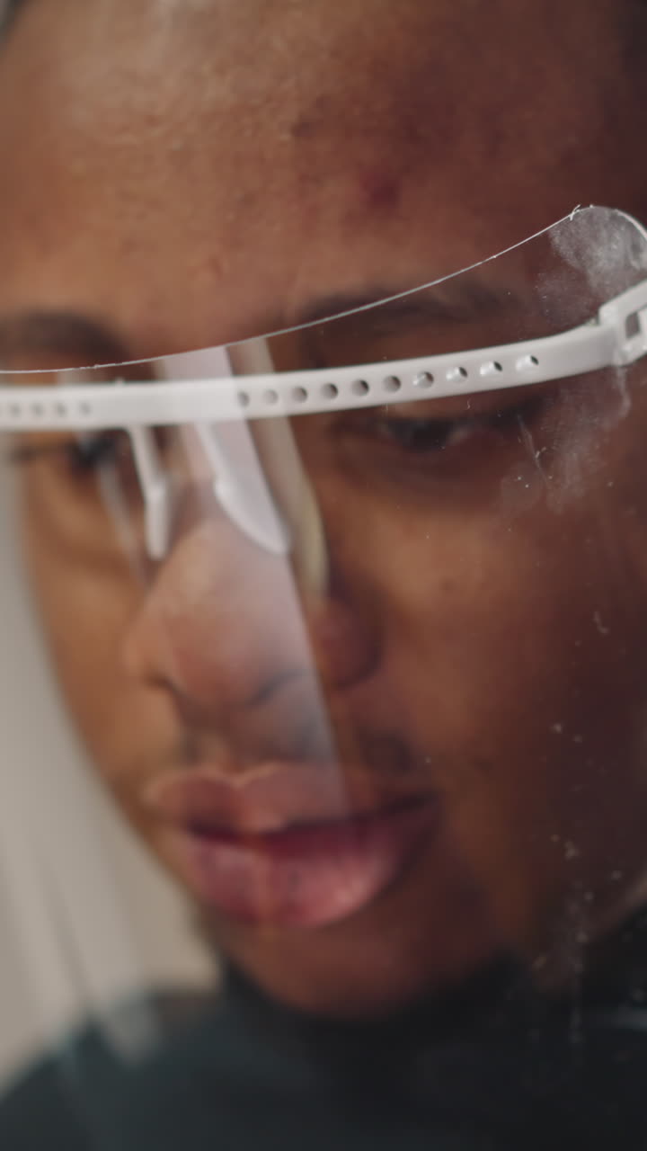 Concentrated young African-American bearded man with protective face shield works on tablet computer standing in light studio extreme closeup