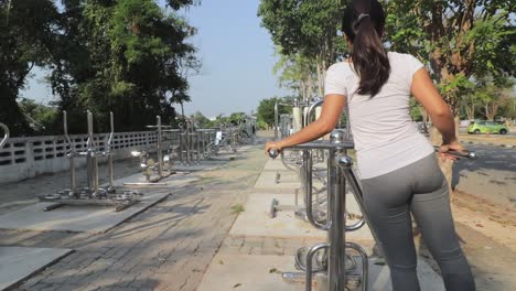 Una-Mujer-En-Un-Equipo-De-Balanceo-En-Un-Gimnasio-Al-Aire-Libre-En-Tailandia,-Tonificando-Sus-Caderas-Y-Cintura---Toma-Amplia