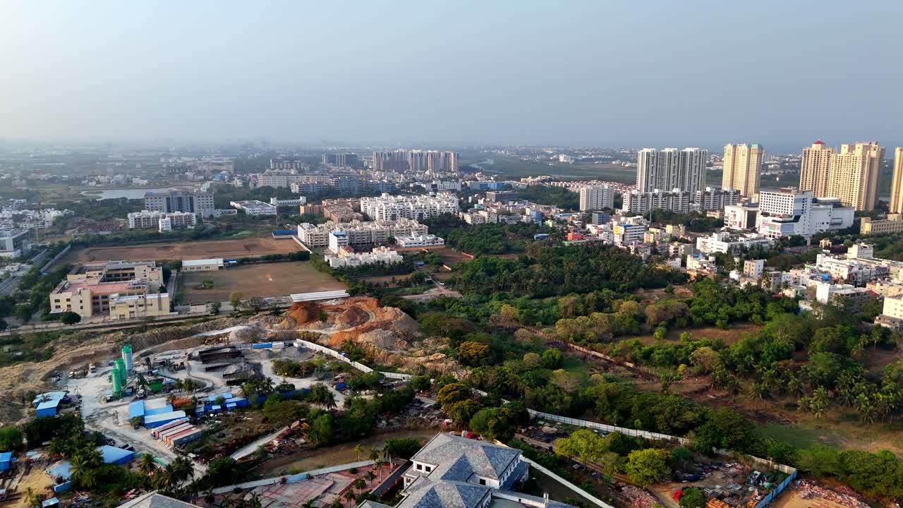 Aerial view of Chennai's urban sprawl, OMR area. Shows mixed development: modern high-rises, ongoing construction, green patches, and older structures.