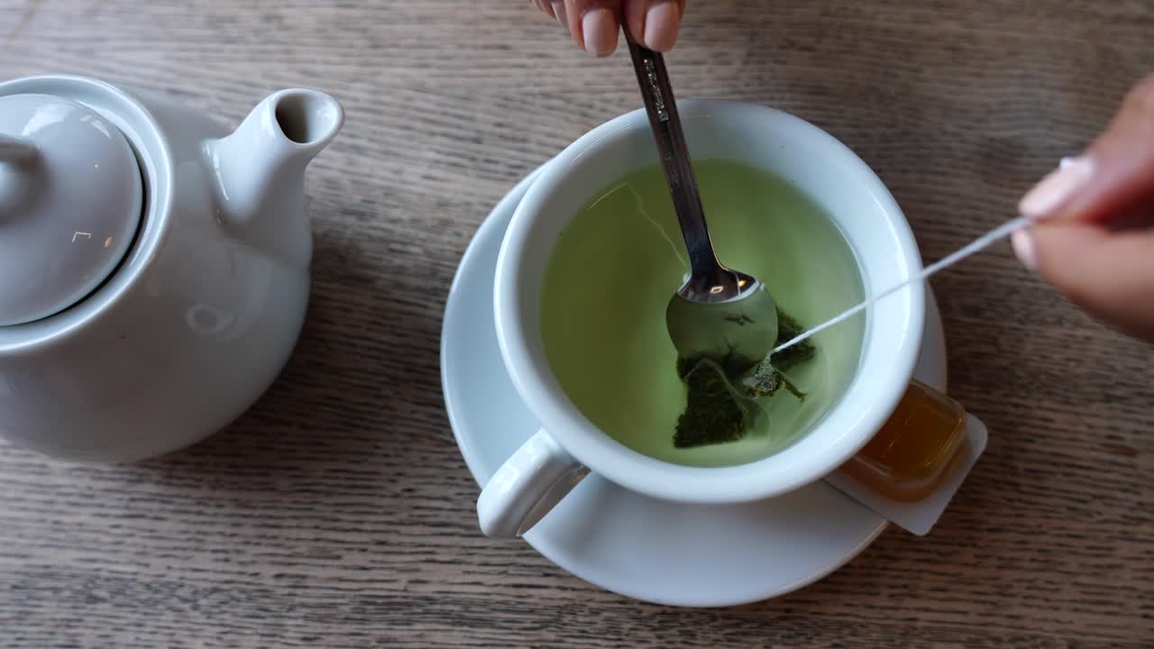 la mano de la niña manicure sostener la bolsa de té verde en una taza de cerámica y agitar en agua