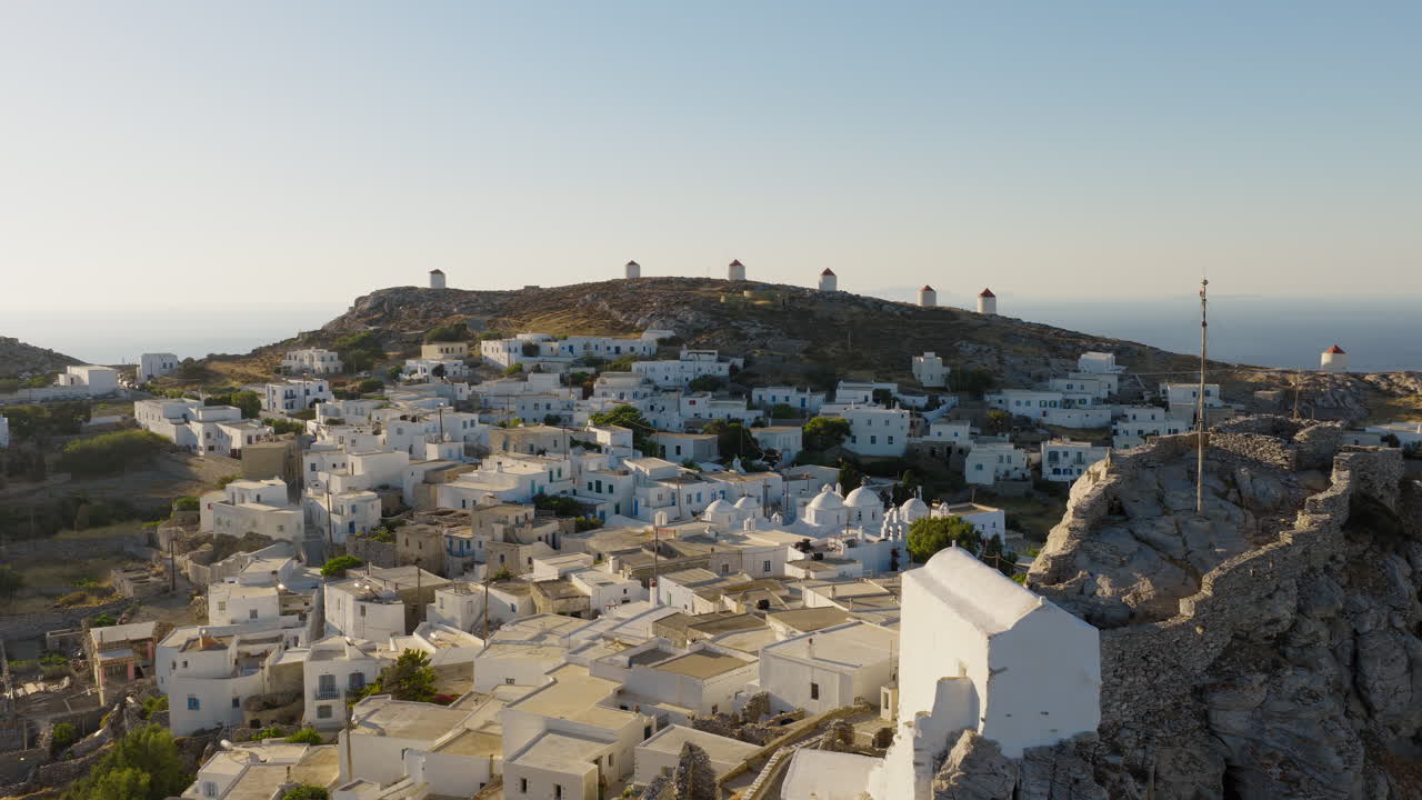 Early morning aerial of Chora town on Amorgos Island with sunlit rooftops and hills, slow drone approach