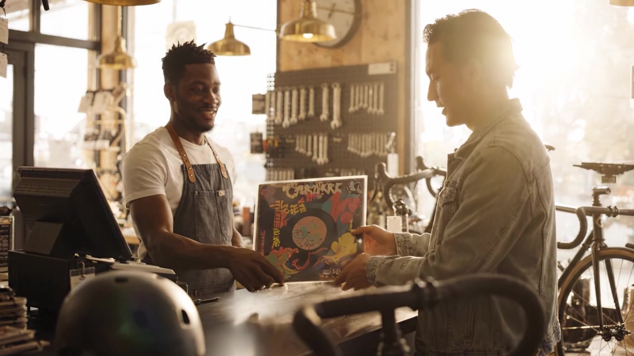 A Vibrant Moment in a Cozy Bike Shop: Engaging Conversations Over Vintage Records and Cycling Gear with a Friendly Attitude and Warm Ambiance