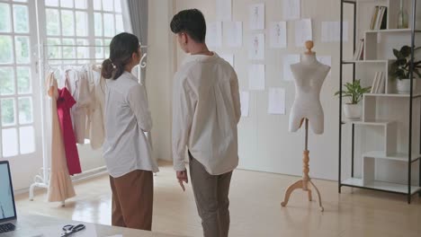 female and male fashion, designer, choosing and pinning to the wall clothing sketches for their new collection