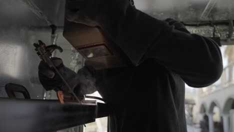 Welder-welding-carefully-metal-construction-shield-mask-indoors-workshop-factory