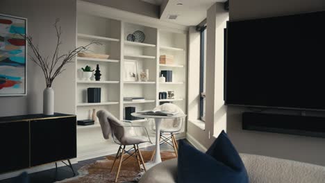 a cozy reading area with large neatly decorated white shelving, 2 chairs, and a small white table