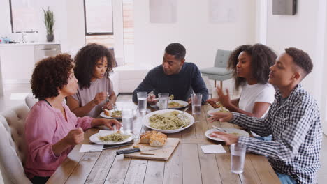 Elevated-view-of-black-family-sitting-at-dinner-table-talking-as-they-eat-together,-close-up