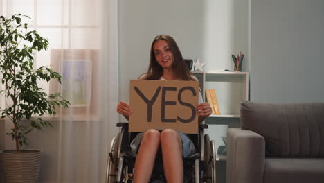 Happy-woman-sits-in-wheelchair-holding-poster-with-word-Yes