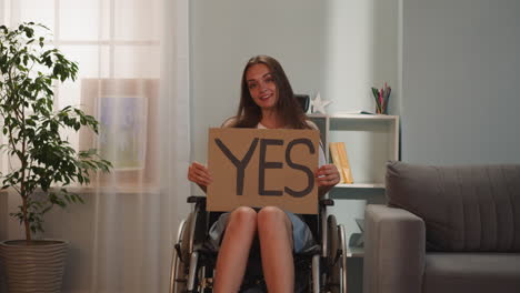 una mujer feliz se sienta en una silla de ruedas sosteniendo un cartel con la palabra sí