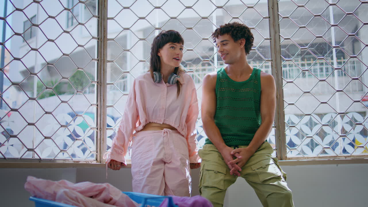 우호적인 소녀는 세탁 바구니에서 남자와 얘기합니다. 행복한 젊은 커플은 기다리고 유혹합니다.