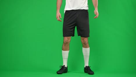 unrecognizable caucasian sportsman catching passing ball in slow motion on green screen. young professional footballer playing game at chromakey background.