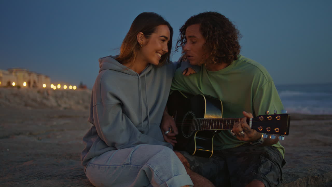 Couple jouant de la guitare sur la plage au coucher du soleil