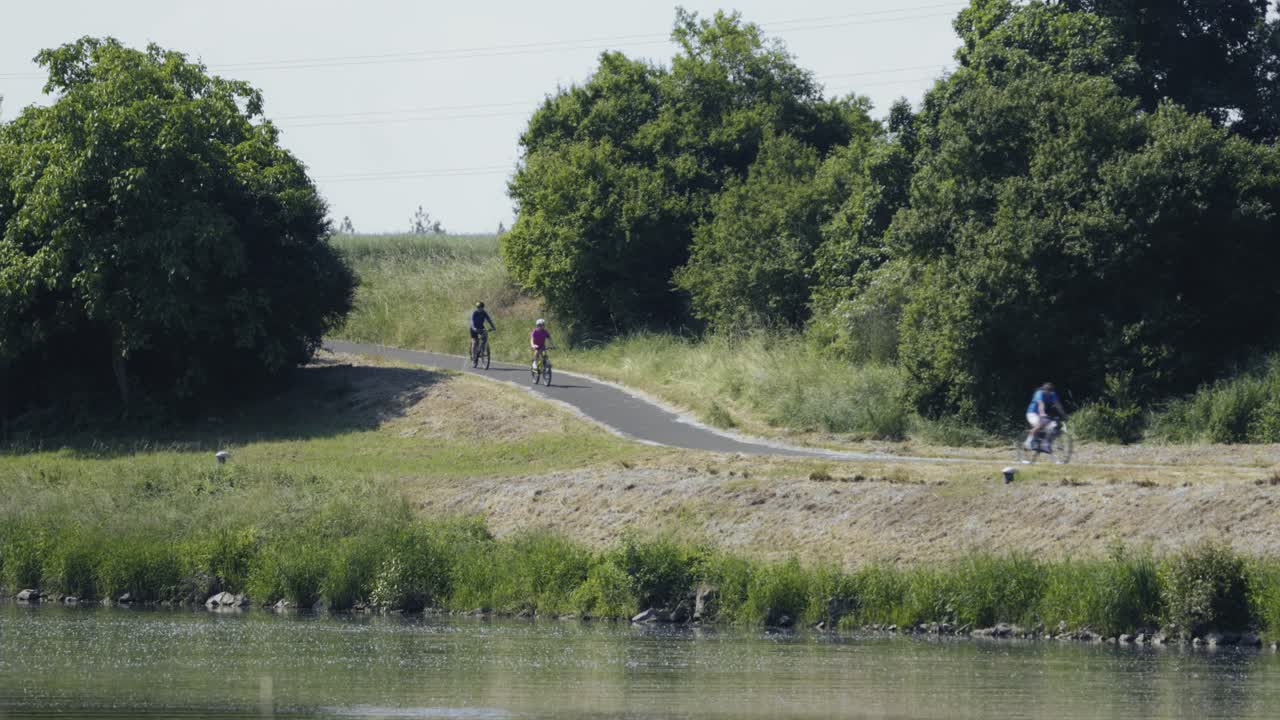 Asfaltcykelsti langs floden og cyklister, der nyder en solrig dag.