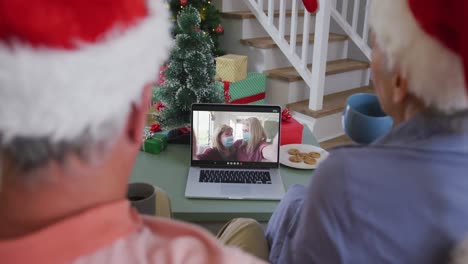 Glückliches-älteres-Kaukasisches-Paar-Bei-Einem-Videoanruf-Auf-Dem-Laptop-Mit-Freundinnen-In-Gesichtsmasken-Zu-Weihnachten