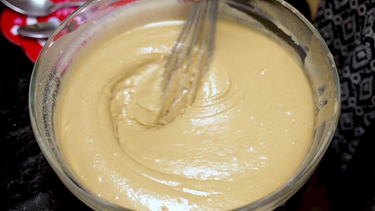 Whisking smooth cake batter in a glass bowl, mixing ingredients for baking delicious homemade desserts in the kitchen