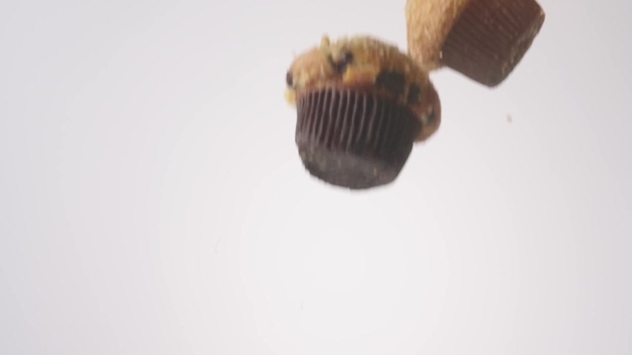 Muffin dorati con frutti di bosco che cadono a cascata e si riversano nell'inquadratura su sfondo bianco, al rallentatore. Ideale per post di brunch del weekend, contenuti per colazioni salutari, contenuti per la festa della mamma.