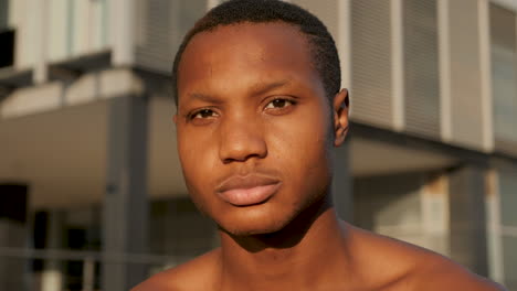 portrait of young black man looking at camera outdoors. shirtless handsome african american male athlete resting on a sunny afternoon. close-up.