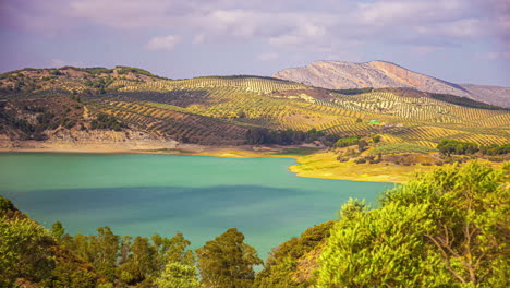 Zeitrafferaufnahme-Der-Wolkenbewegung-über-Dem-Stausee-El-Limonero,-Umgeben-Von-Grüner-Landschaft-Entlang-Hügeligem-Gelände-In-Malaga,-Spanien