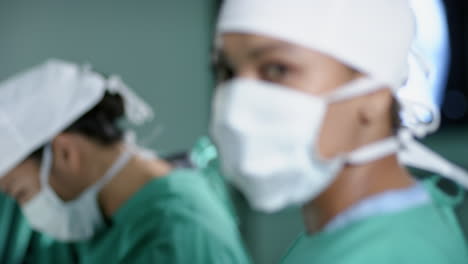 Portrait-of-biracial-female-surgeon-wearing-face-mask-in-operating-theatre-at-hospital,-slow-motion