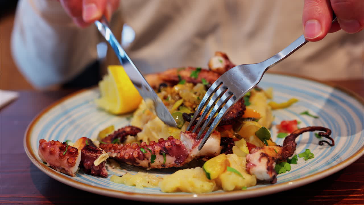 Close up of a man cutting and eating grilled octopus on a puree at a restaurant