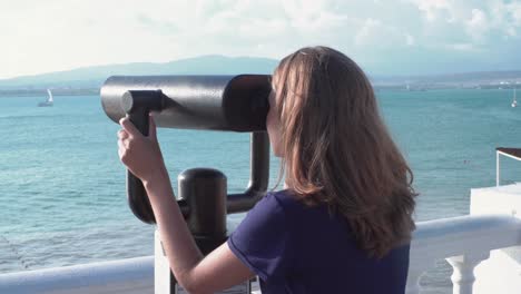 girl looking through a telescope at the sea