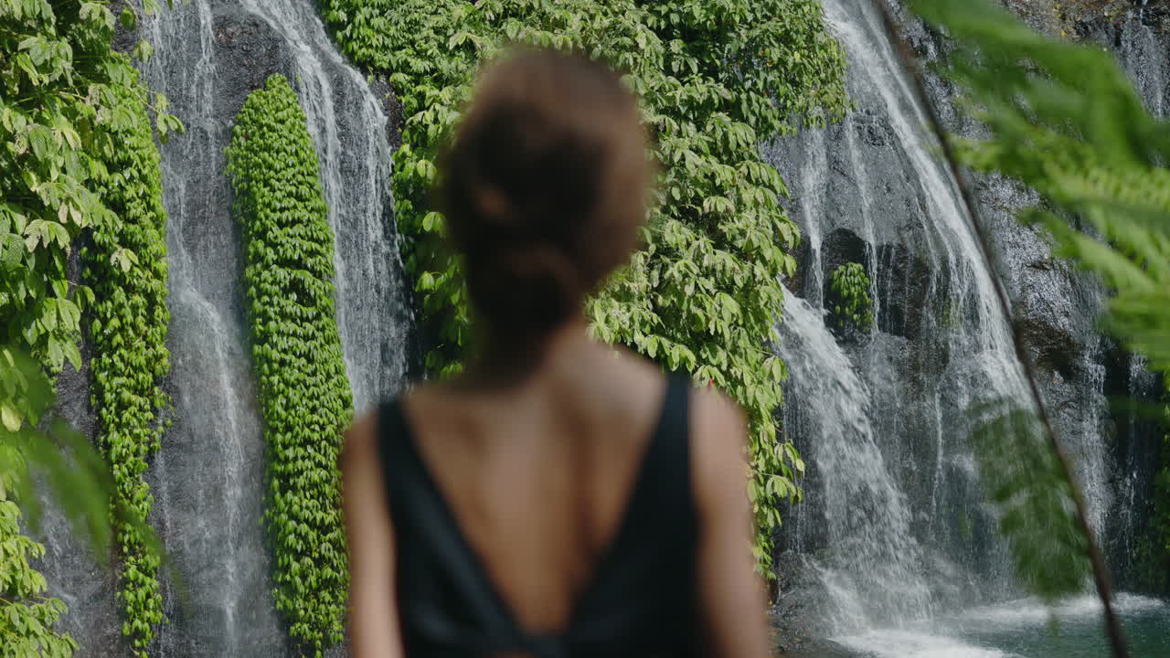 Blurred Woman from Behind Gazing at a Lush Green Waterfall