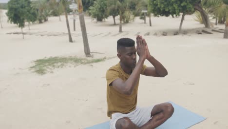 un hombre afroamericano relajado practicando meditación de yoga sentado en la playa, en cámara lenta.