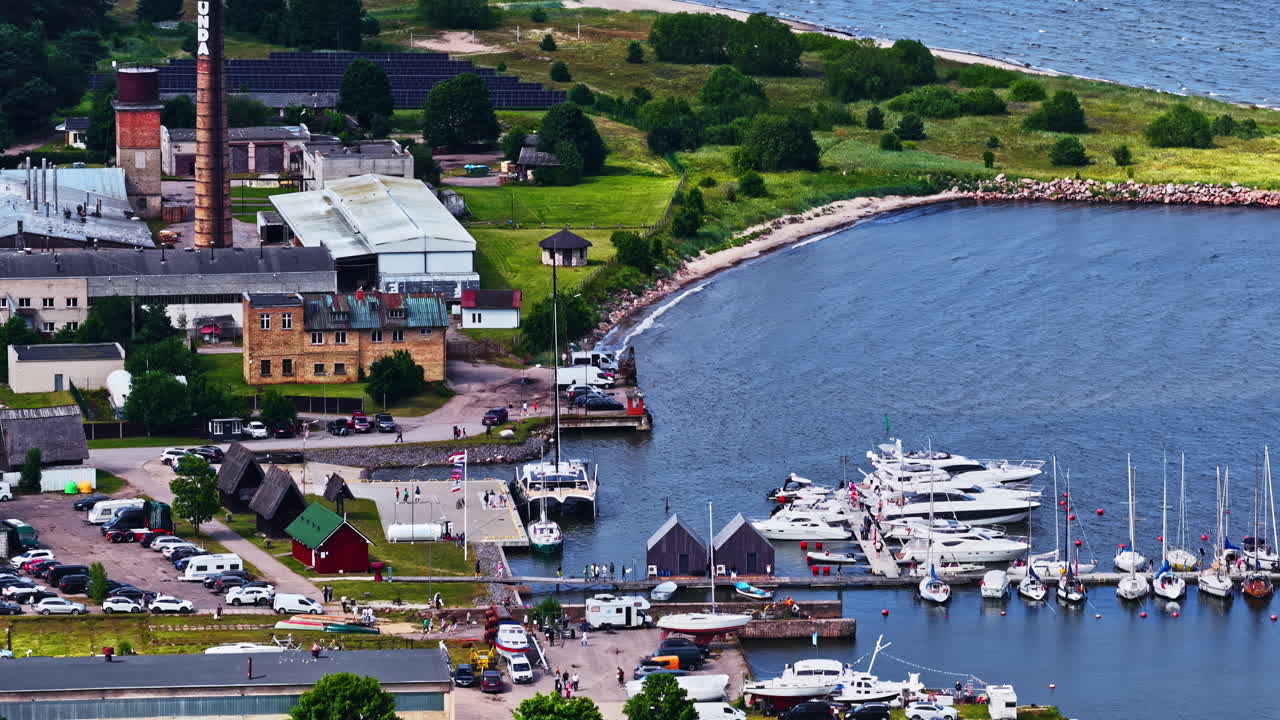 Drone aerial of boats docked in protected harbor at bay beside buildings and blue water