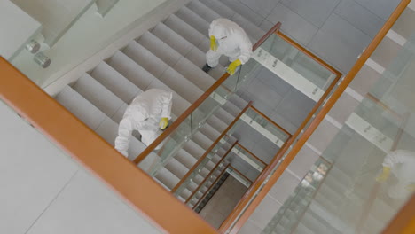 top view of two cleaning men wearing personal protective equipment cleaning stair railings inside an office building 1